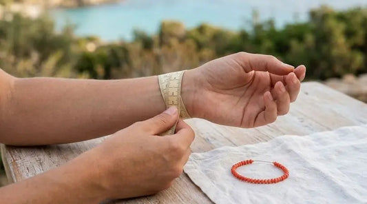 Mesure d’un poignet avec un mètre ruban, à côté d’un bracelet en perles de corail rouge posé sur un tissu blanc.